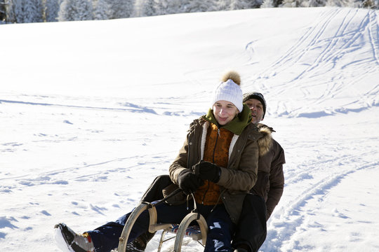 Senior couple sitting on sledge looking at camera smiling, Sattelbergalm, Tyrol, Austria