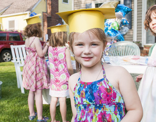 Portrait of young girl at kindergarten graduation, wearing paper mortar board