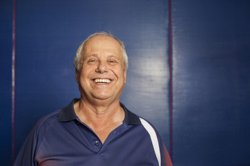 Portrait of senior man (table tennis player) wearing navy blue polo shirt looking at camera smiling