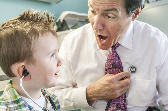 Male doctor letting young boy play with stethoscope in doctor's office
