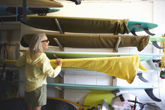 Senior woman taking surfboard from shelf