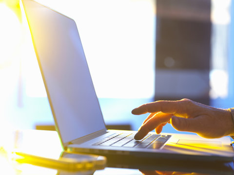 Businessman typing on laptop computer in office with sunlight coming through window