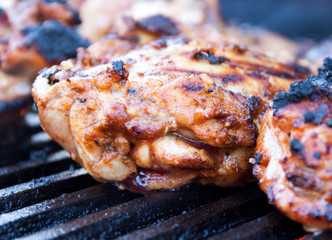 Angled view of seasoned and marinated chicken thighs grilling on hot iron grates over charcoal