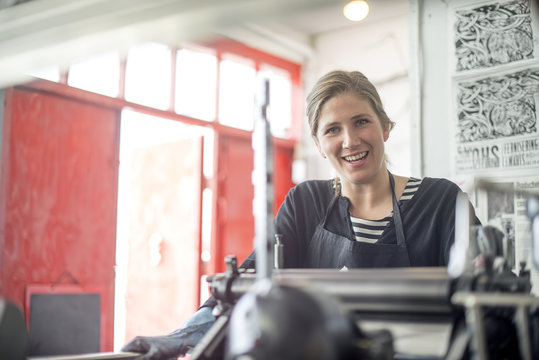 Portrait of female printer with traditional letterpress print machine in workshop
