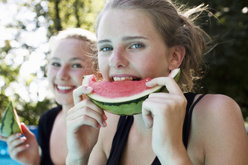 Two teenage girls eating watermelon slices in garden