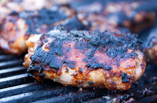 Closeup Of Charred And Seasoned And Chicken Thighs Being Grilled On Iron Grates Over Charcoal