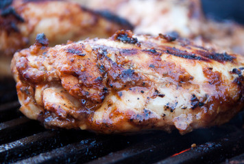 Closeup of seasoned and marinated juicy chicken thighs being grilled on iron grates over charcoal