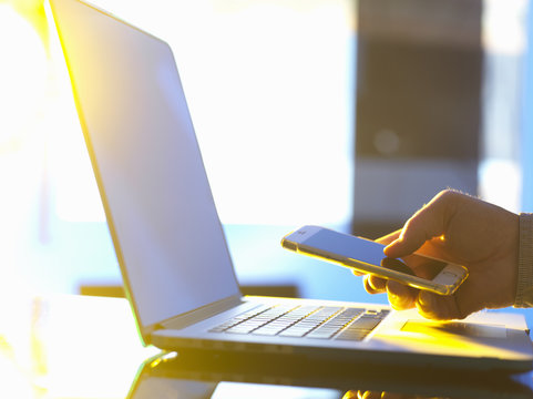 Business man at laptop computer with smartphone in office with sunlight coming through window