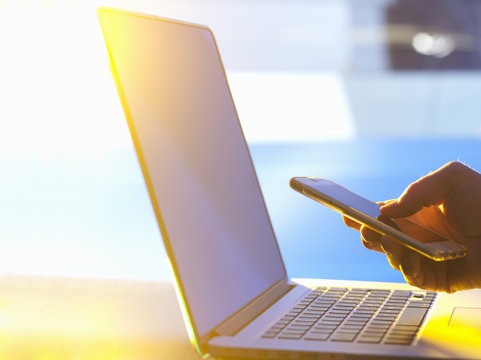 Business man at laptop computer with smartphone in office with sunlight coming through window