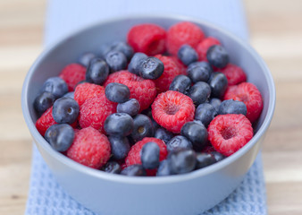Dessert fresh berries in the bowl. Raspberries and blue-berries on a wooden table. Dessert, fresh berries close-up. 