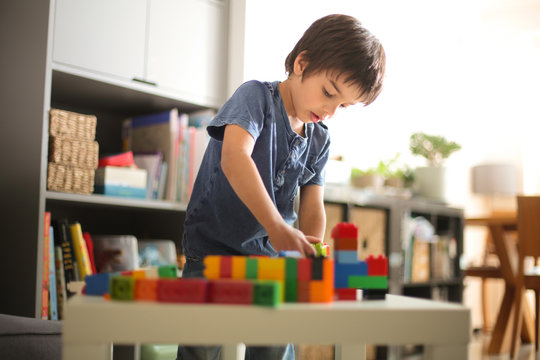 Boy at home looking down playing with colourful building blocks