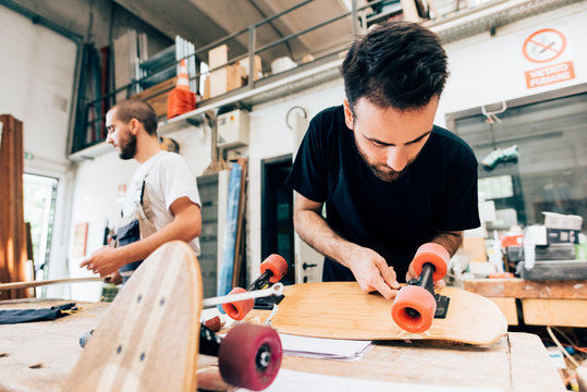 Young man in carpentry workshop attaching wheels to skateboard