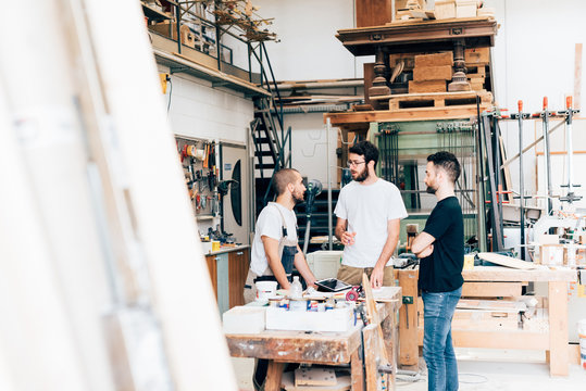 Friends standing around workbench in carpentry workshop talking