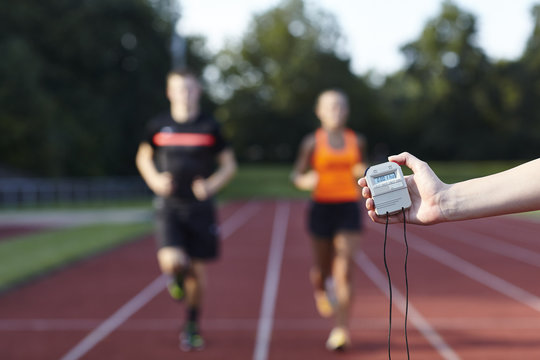 Young man and woman running on race track against stopwatch