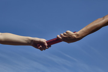 Hands of female relay runners passing baton against blue sky
