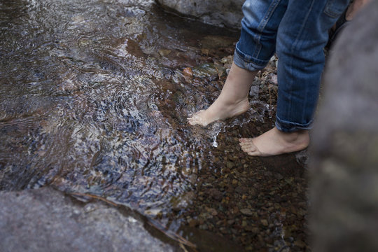 Legs and bare feet of female toddler dangling over rockpool