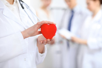 Female doctor with stethoscope holding heart.  Two doctors standing in the background