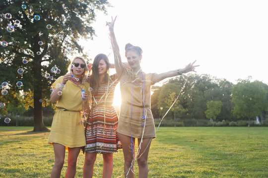 Portrait of three young women friends wrapping themselves in streamers at party in park