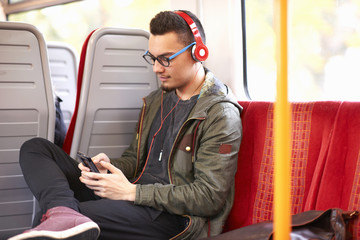 Young man sitting on train, using smartphone, wearing headphones