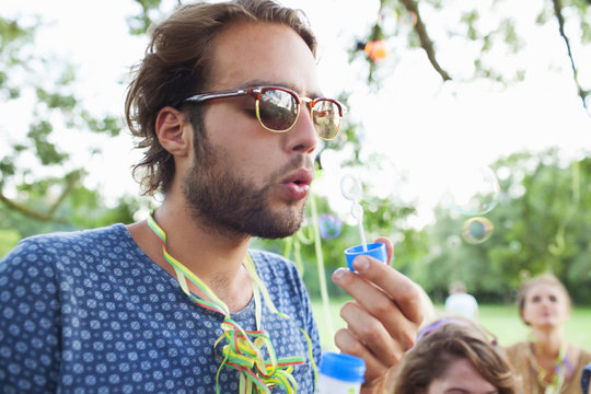 Young man blowing bubbles at sunset party in park