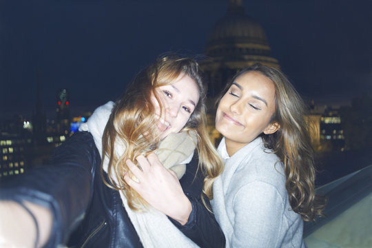 Two young women taking selfie in front of St Pauls at night, London, UK