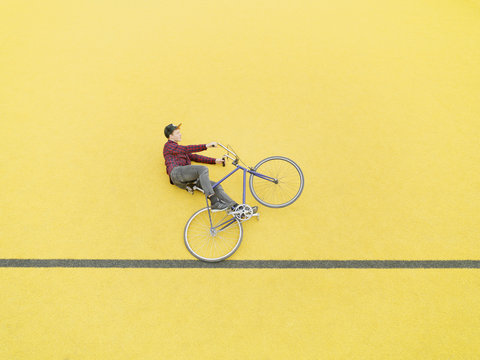 Urban cyclist doing illusionary stunt against yellow wall