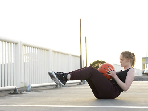 Young female basketball player doing sit-ups in parking lot