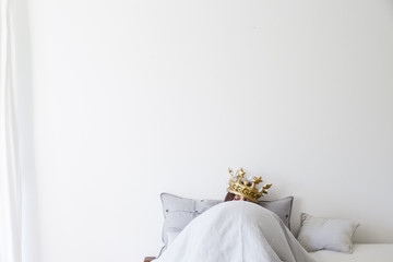 Mature woman in bed underneath quilt wearing golden crown