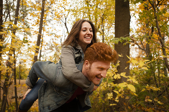 Young man giving girlfriend a piggy back through autumn forest