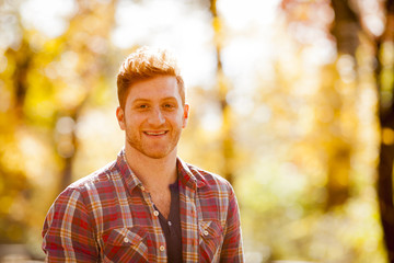 Sunlit portrait of red haired young man in forest