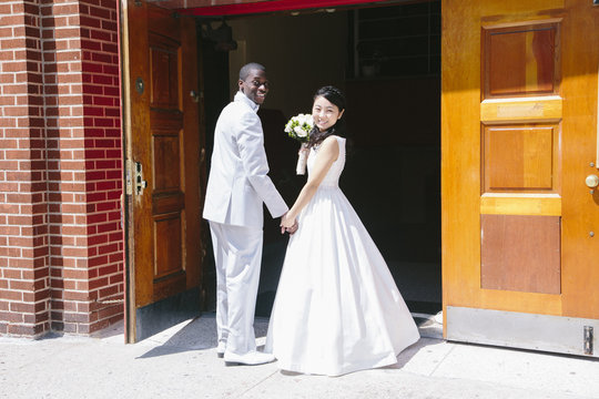 Side view of bride and bridegroom standing at church doors looking at camera smiling