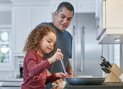 Father helping daughter cook on hob in kitchen