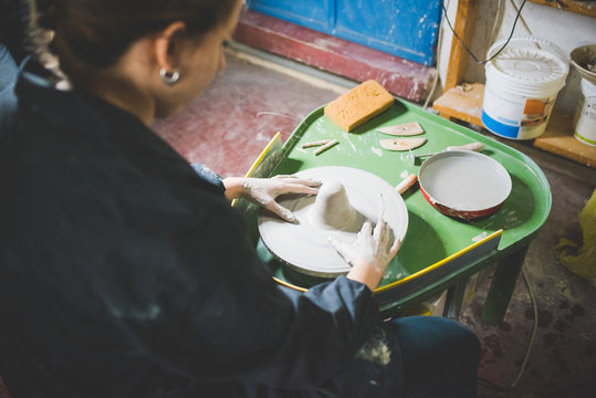 Over shoulder view of young woman sitting using pottery wheel