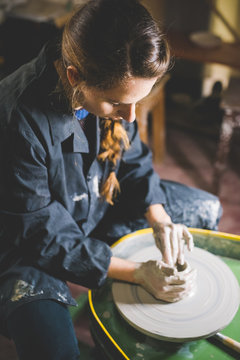 Young woman sitting at pottery wheel shaping clay
