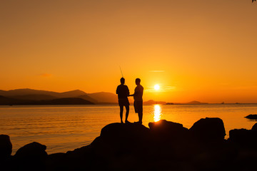 Couple love standing on the stone fishing at sea sunset backgrou