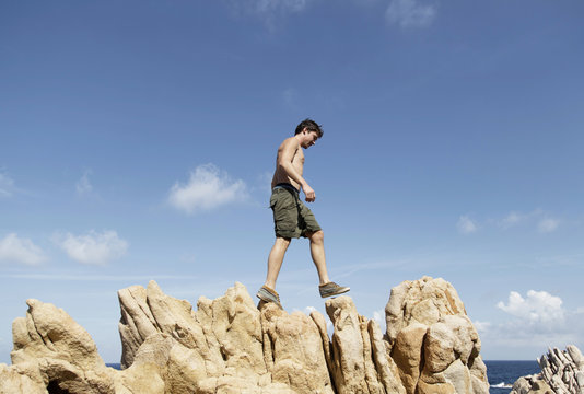 Low angle side view of young man climbing on rocks, Costa Paradiso, Sardinia, Italy