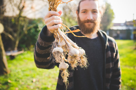 Bearded mid adult man in garden holding freshly picked garlic bulbs looking at camera smiling
