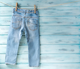 Baby boy blue jeans hanging on a clothesline on blue wooden backgroung