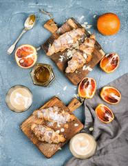 Traditional Italian style home breakfast. Latte in glasses, almond croissants on rustic wooden boards and red bloody Sicilian oranges over concrete textured table
