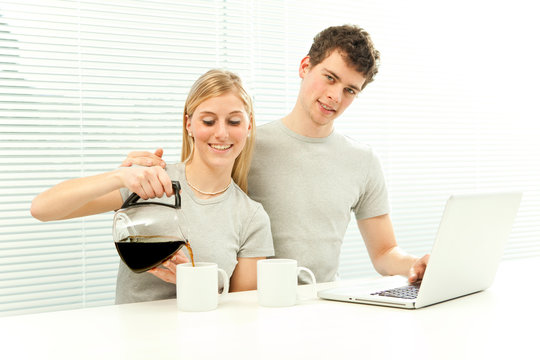 Young casual couple have breakfast with coffee and fruit laptop with venetian blind window