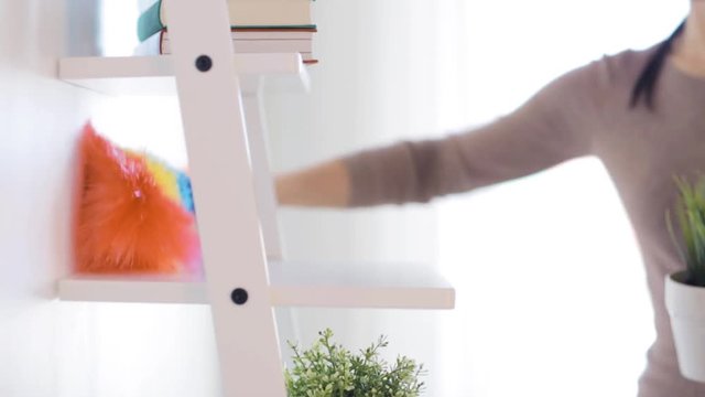 woman with duster cleaning dust from shelf at home