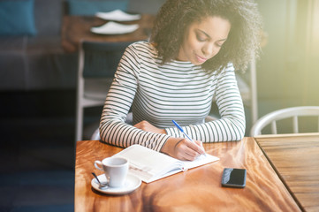 Beautiful african girl is making notes in cafeteria