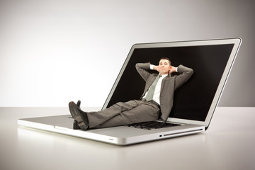 Little relaxed businessman lie on giant laptop at work