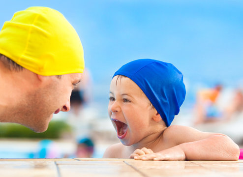 happy child and dad with swimming pool cap have fun in a pool