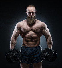 Fototapeta na wymiar Bearded Muscular bodybuilder posing with heavy dumbbells