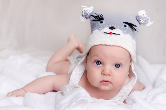 Little boy in a funny wool hat with mug animal on white sheet