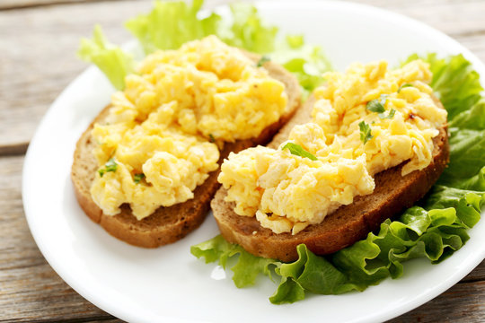 Scrambled eggs with bread and vegetables on a grey wooden table