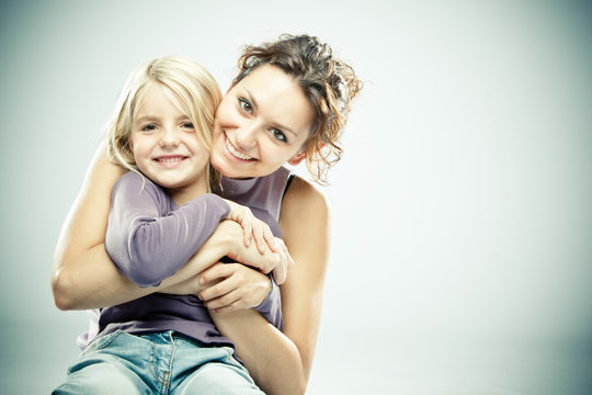 Beautiful brunette woman with young blond girl on grey background