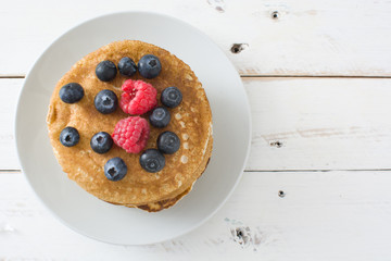 Pancakes with blueberries and raspberries on white wood
