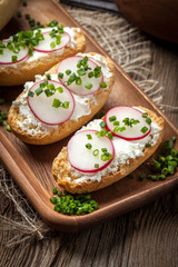 Toasts with radish, chives and cottage cheese on a wooden table.